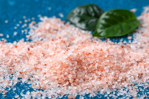 Pink coarse salt crystals on a blue table. Himalaya salt. Background for advertising salty.