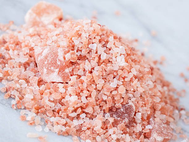 Natural light photo of pile of coarse ground Himalayan Pink Salt and large chunks on marble table.